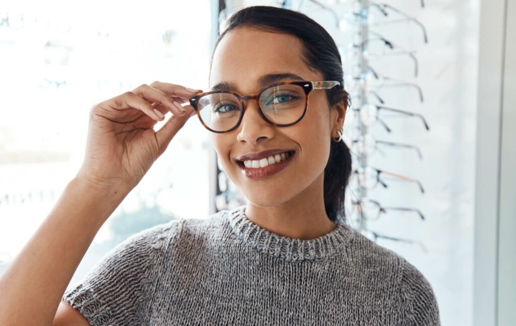 A person smiles widely as they try on the perfect pair of glasses